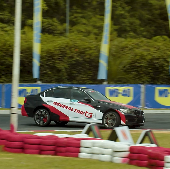 Imagem mostra uma BMW adesivada com a marca General Tire realizando manobras de derrapagem em uma pista asfaltada. A pista conta com zebras e pneus para proteção nos arredores.