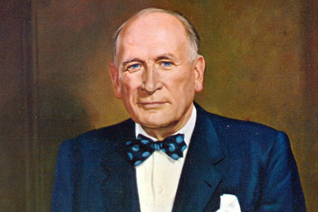 Imagem - Sobre a Marca General Tire Imagem de um retrato de William F. O'Neil, fundador da marca General Tire, vestindo um terno azul escuro com gravata borboleta de bolinhas. Ele tem uma expressão serena, com olhos azuis claros e cabelos grisalhos. Ao fundo, o retrato possui um tom de cor neutra. Este retrato parece ser uma pintura formal, destacando a figura do homem como alguém de importância ou relevância.