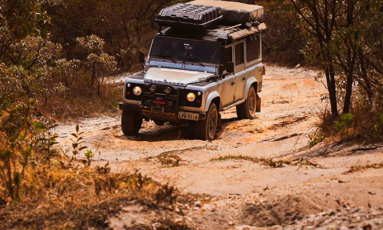 Imagem de uma Land Rover Defender equipada com 4 pneus General Tire Grabber X3. O veículo está subindo uma estrada de terra não pavimentada no meio de uma vegetação de serrado.